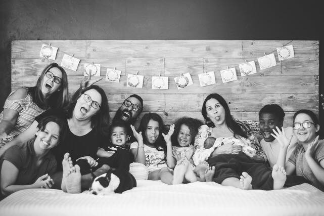 Family celebrating birth of new baby with bible verses for labor and delivery strung on headboard above everyone's heads.