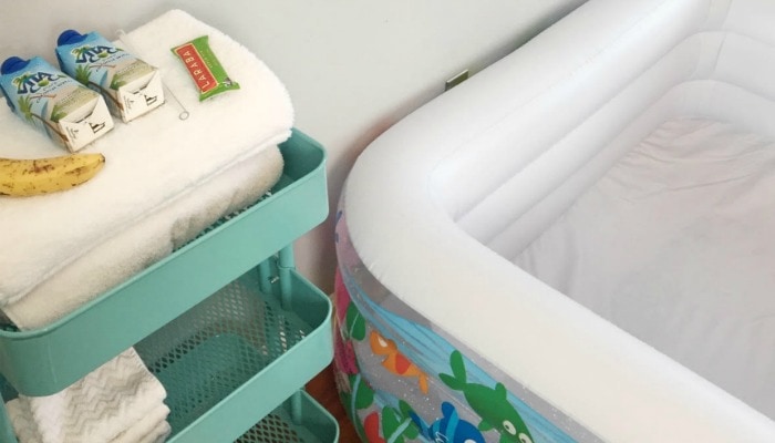 Teal cart with white towels and birthing snacks next to an empty fishy birthing pool, a childbirth assistant emptied after birth.