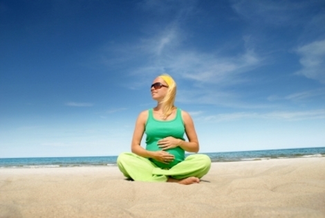 pregnant woman wearing green sitting cross legged on the beach