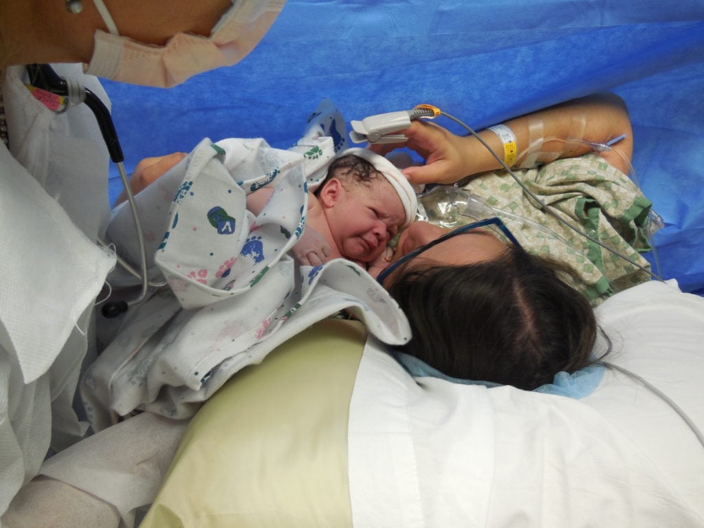 mom touches and kisses baby immediately after birth during a gentle c section delivery