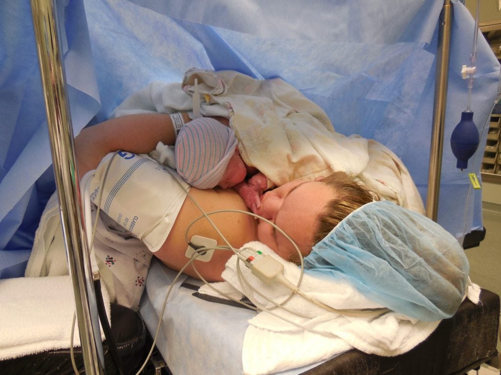 mom kissing baby's fingers in OR after cesarean delivery under blue drape