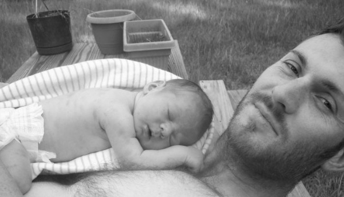 dad with no shirt holding newborn in diaper outside