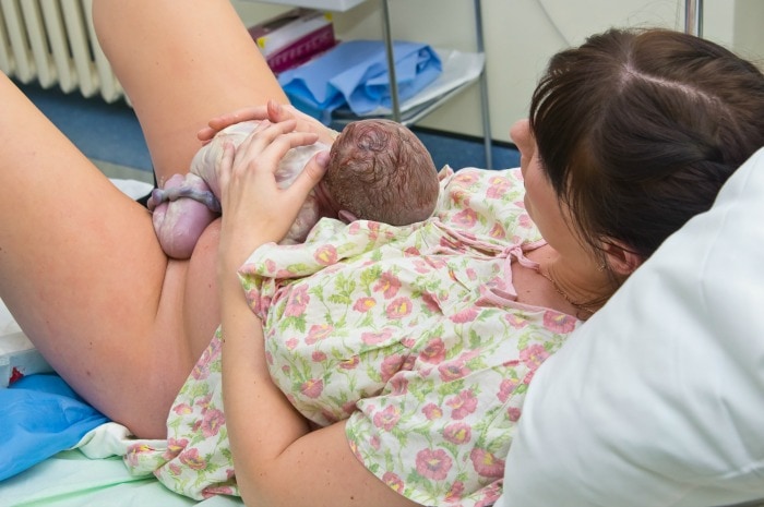 Mother holds baby while baby receives delayed cord clamping during the third stage of labor.