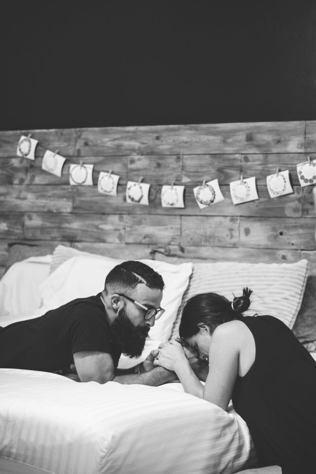 Family using printable birth scriptures during labor while woman kneels next to bed during a contraction while holding her husband's hand. 