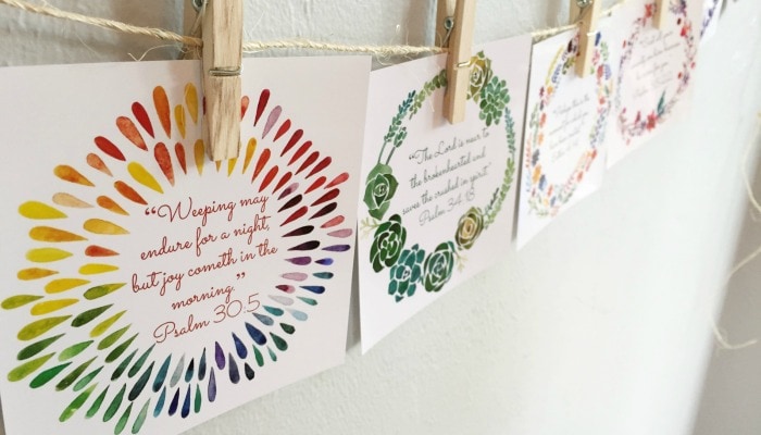 Vibrant, beautiful birth scriptures hung by clothespins on a long piece of twine. Bible verses for labor and delivery are hung on a wall during pregnancy to prepare for birth. 