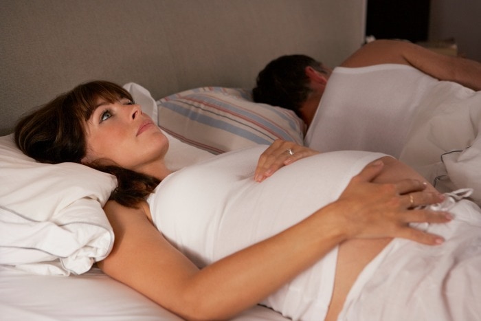 pregnant woman experiencing insomnia while her partner sleeps next to her in bed