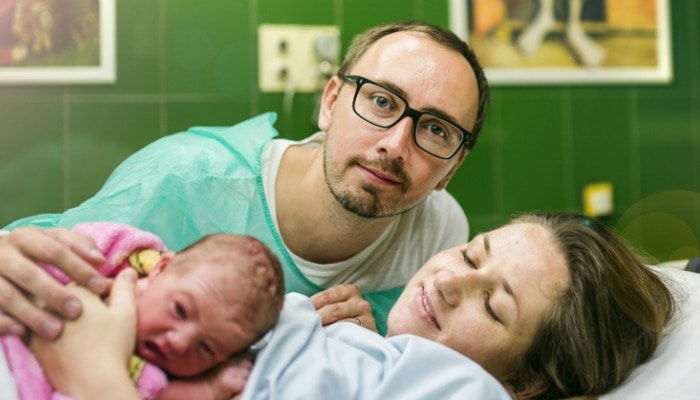 newborn baby receiving skin-to-skin with mother while father looks on