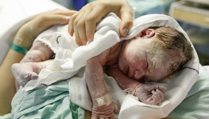 mother holds newborn baby covered in vernix during the third stage of labor