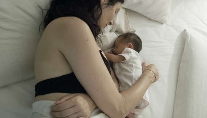 woman lying in white bed with newborn