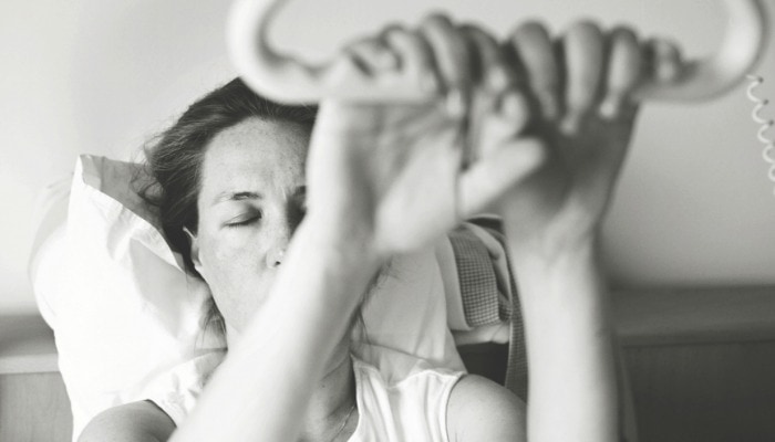 Pregnant woman coping in hospital bed during contraction by holding on to handle.