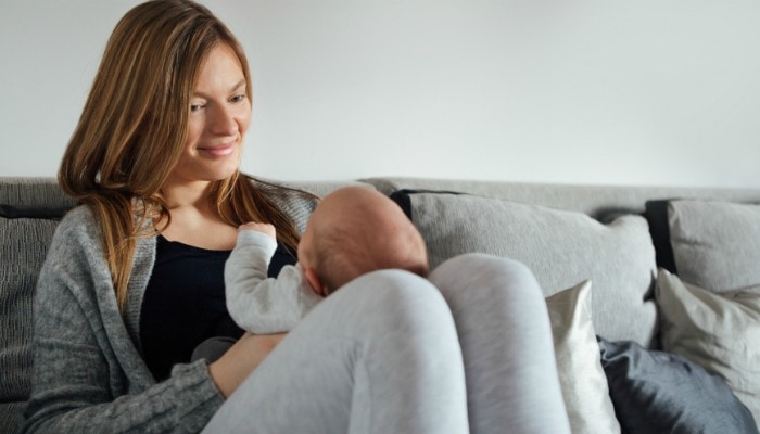 new mom sitting on grey couch holding newborn on knees propped up