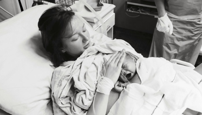 Mother holds baby skin-to-skin and touches baby's head during third stage of labor right after birth.