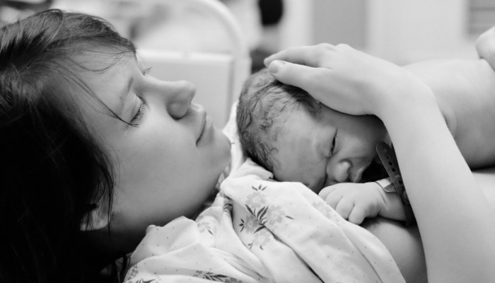 Mother holds newborn baby skin-to-skin during the third stage of labor.