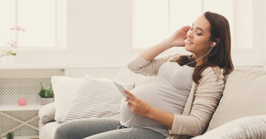 pregnant woman sitting on couch with eyes closed listening to hypnobirthing tracks on headphones