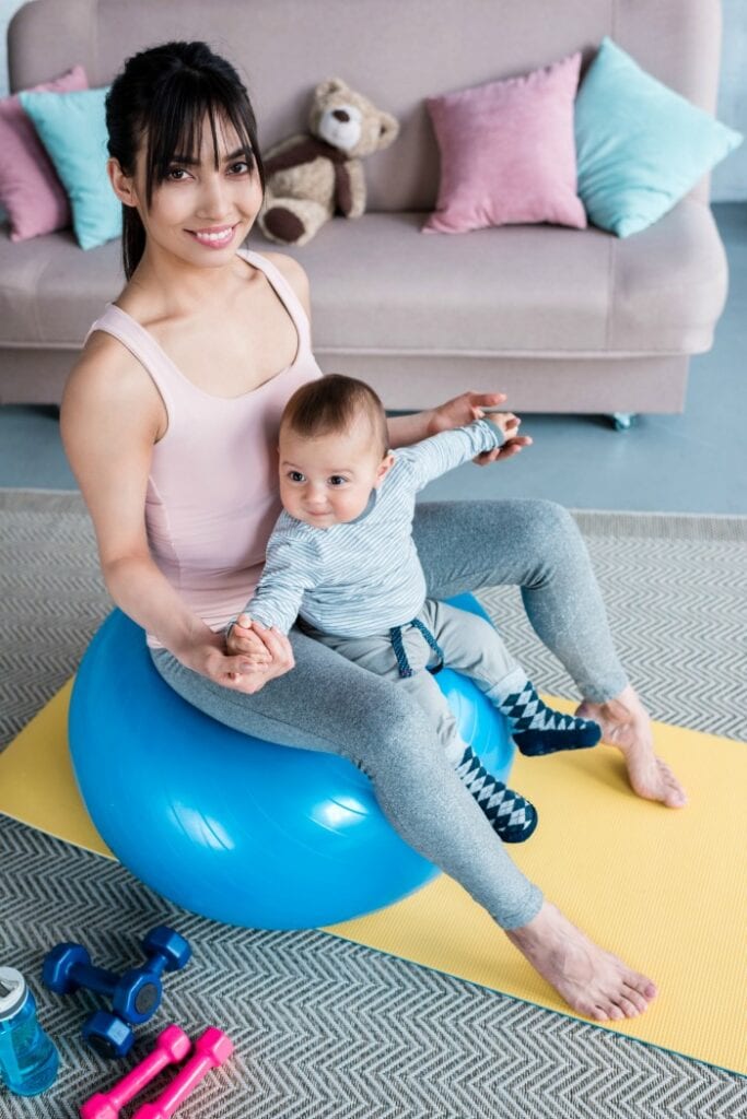 new mom bouncing on yoga ball with baby on lap