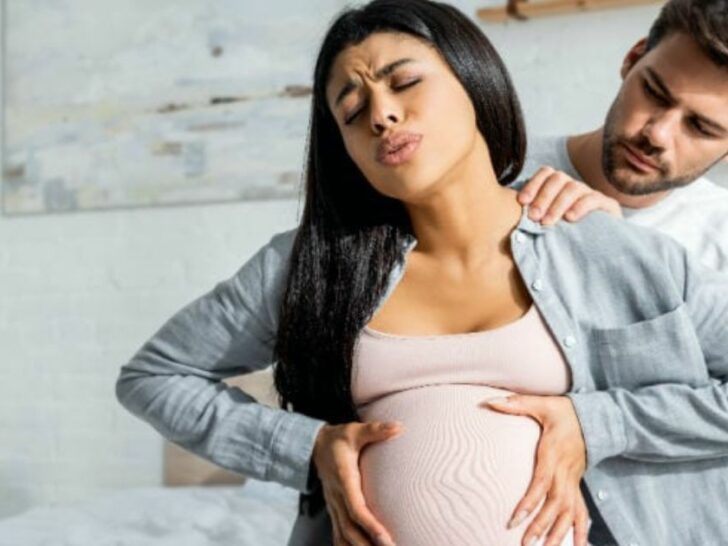 woman in labor holding belly during painful contraction while partner sits behind comforting with hand on her shoulder