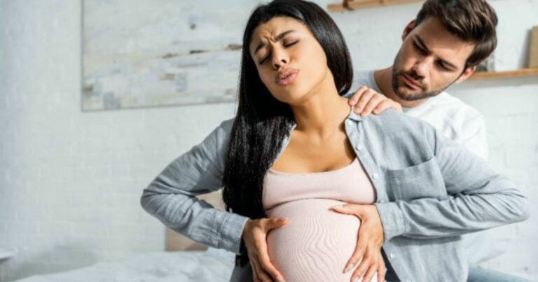 woman in labor holding belly during painful contraction while partner sits behind comforting with hand on her shoulder