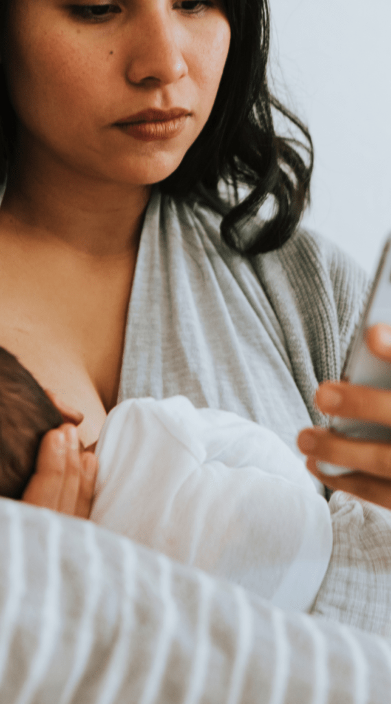 woman breastfeeding infant while looking at her phone