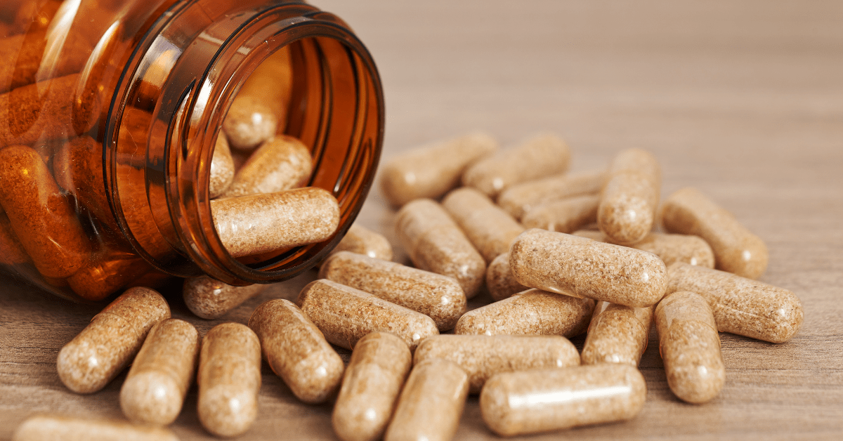 Brown placenta pills spilled out of an amber bottle on a brown surface.