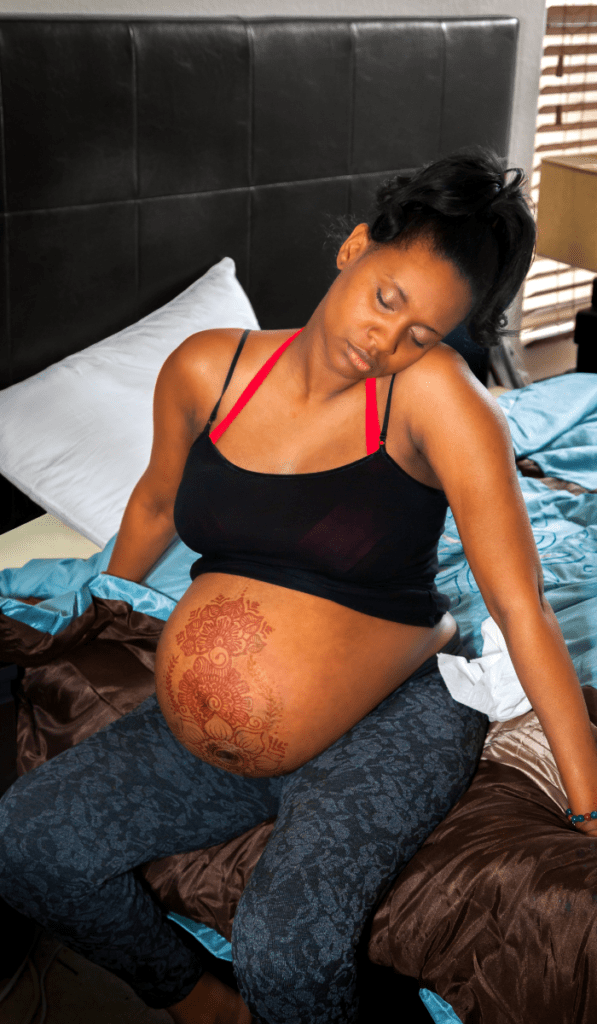 African American woman in labor on bed with henna on belly. She has her mouth, shoulders, and hands relaxed to break the fear tension pain cycle for a better birth. 