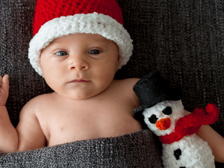 closeup of infant wearing nothing but a knitted pointed red hat with white trim and holding a knitted snowman