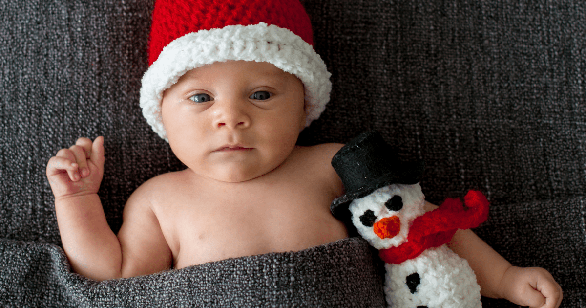 closeup of infant wearing nothing but a knitted pointed red hat with white trim and holding a knitted snowman