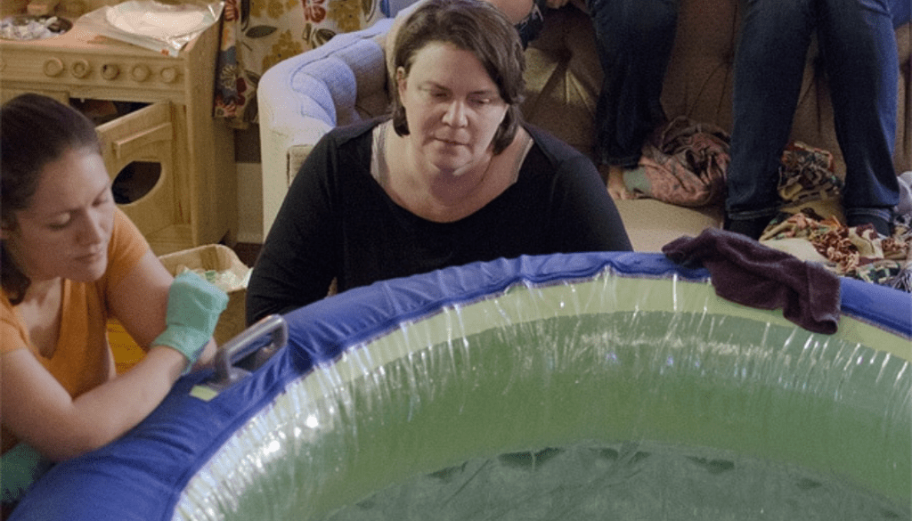 Chidlbirth assistant sitting with midwife next to birth pool at a homebirth while woman gives birth in pool